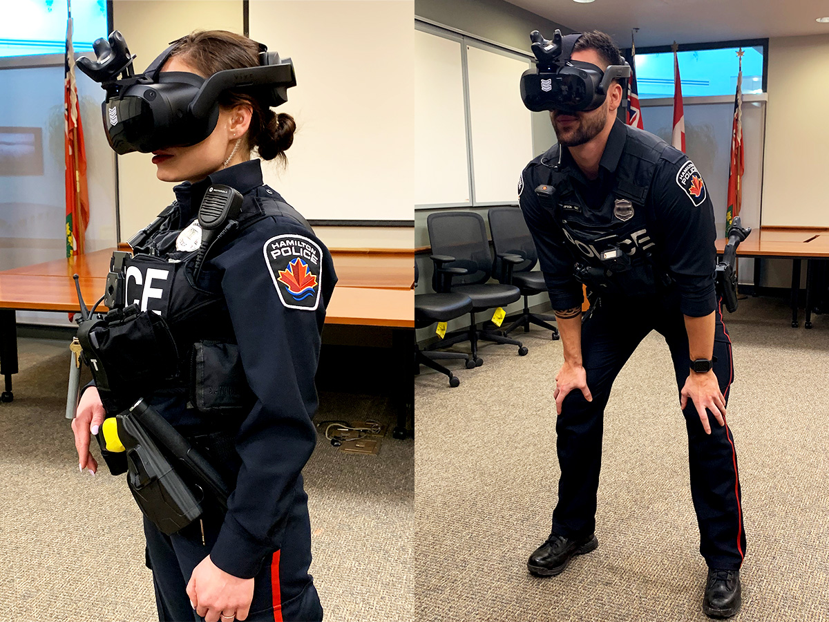 Two police officers, both wearing virtual reality headsets. A female officer is standing while a male officer crouches. 